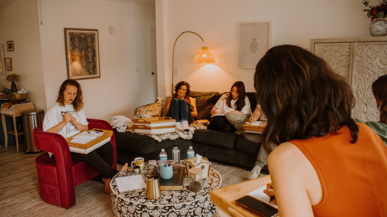 Women gathered in a cozy living room setting for a Love, Lizzy Podcast community workshop, writing and reflecting together on building strong communities, women's leadership, and values-centric living.